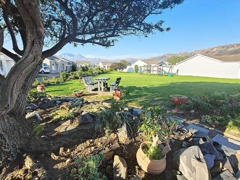 A well-maintained residential garden featuring a mature tree, rockery landscaping, and a spacious lawn with mountain views in the background.