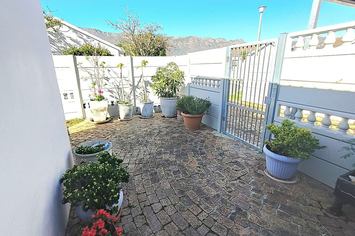 A private rear courtyard featuring cobblestone paving, enclosed by precast concrete walls and a secure metal pedestrian gate.