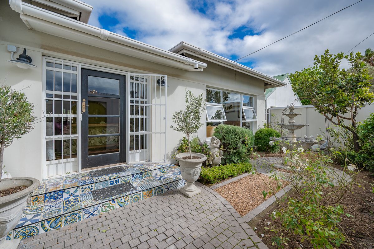 A charming rear exterior view featuring a patterned tiled entrance, paved patio area, and well-maintained garden surroundings.