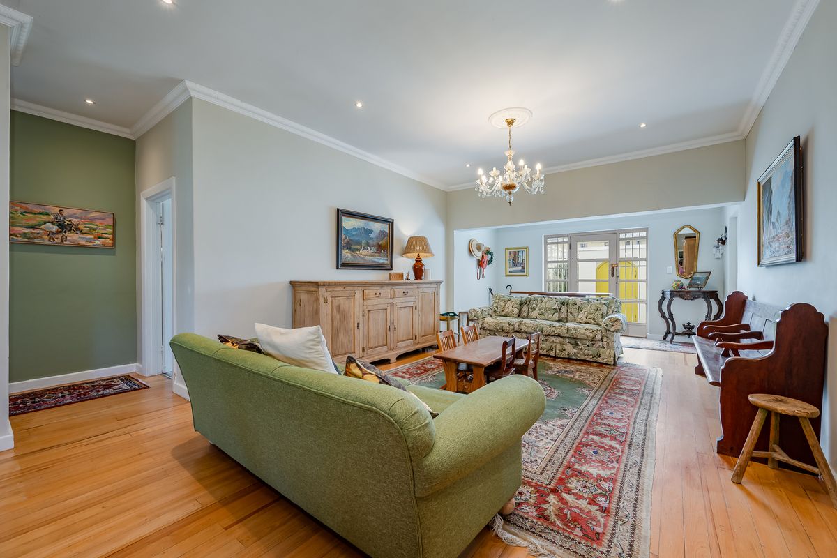 Spacious living room featuring polished hardwood flooring, crown molding, and a classic crystal chandelier, with direct access to the outdoor area through french doors.