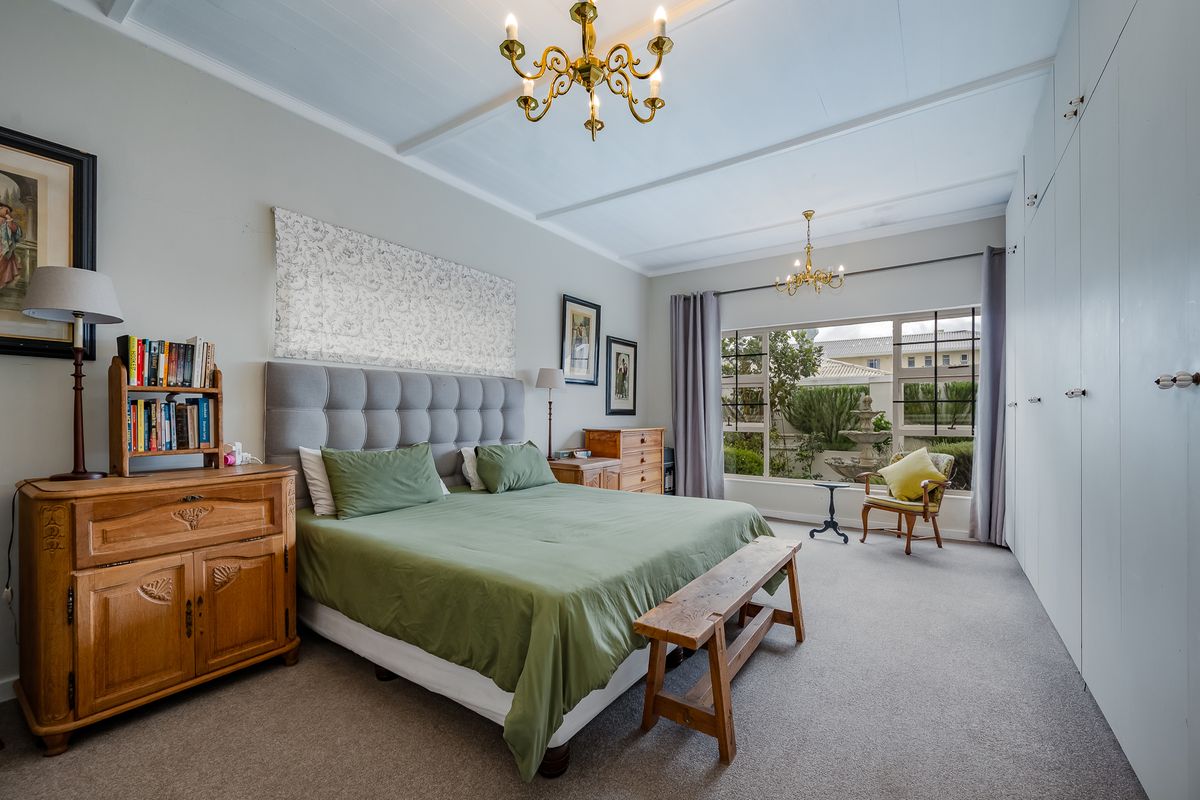 Spacious bedroom featuring built-in cupboards, carpeted flooring, a timber-paneled ceiling, and large windows overlooking the garden.