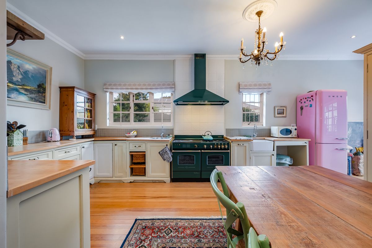A charming kitchen featuring timber countertops, a classic Belfast sink, a green range cooker with matching extractor, and warm timber flooring.