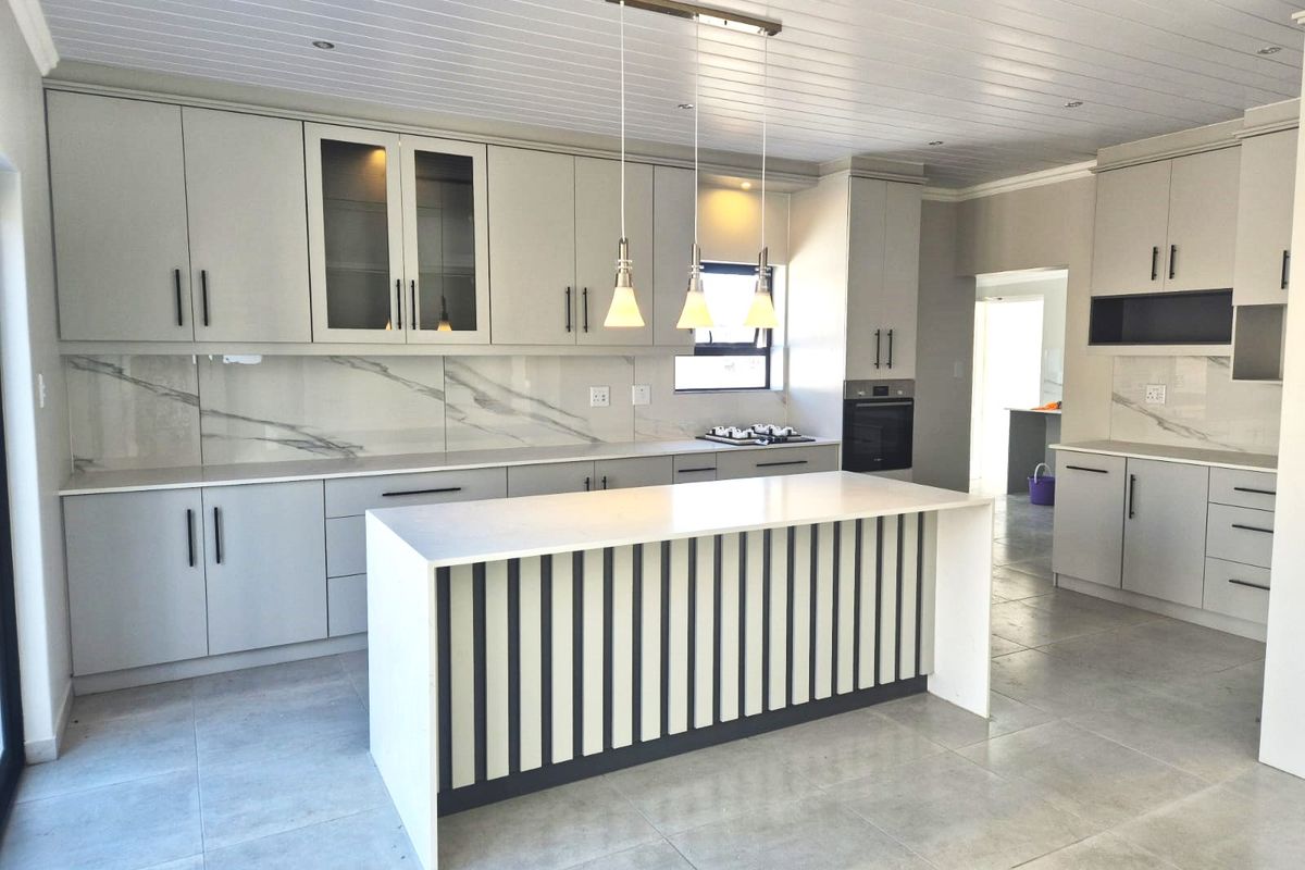 Modern kitchen featuring a central island, stone countertops, marble-look splashback, built-in oven, hob, and stylish pendant lighting with neutral cabinetry.