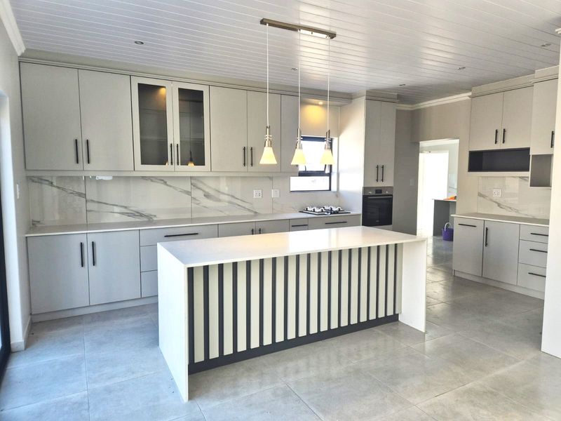 Modern kitchen featuring a central island, stone countertops, marble-look splashback, built-in oven, hob, and stylish pendant lighting with neutral cabinetry.