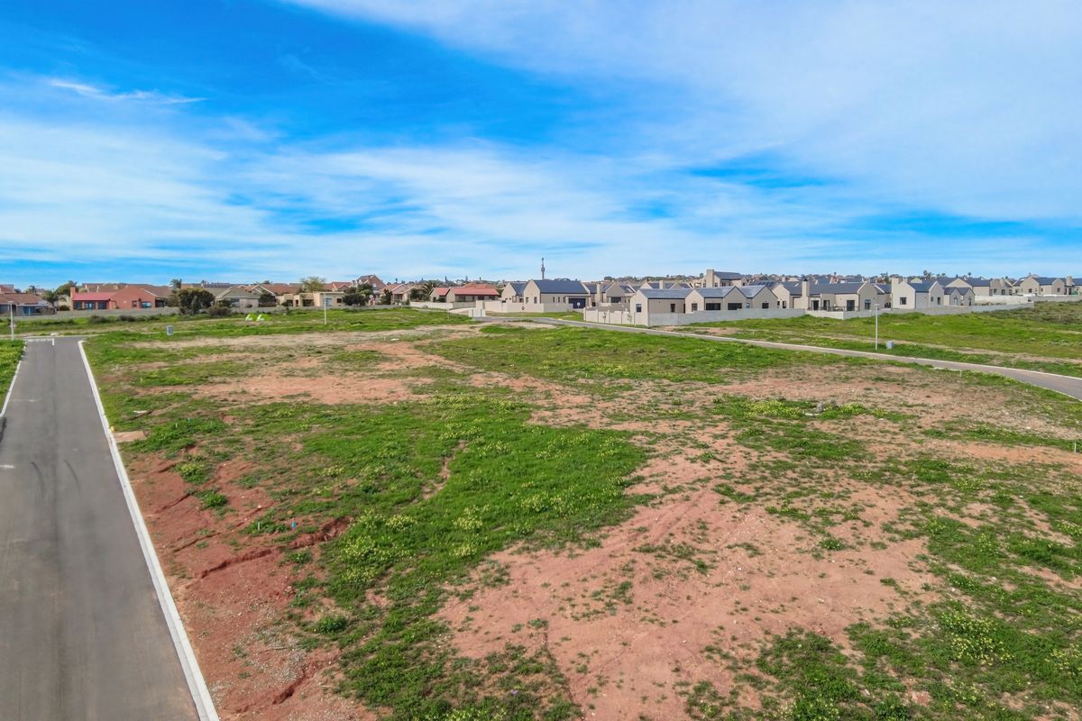 An aerial view of a vacant residential plot situated within a developed estate, featuring paved road access and surrounding neighborhood homes.