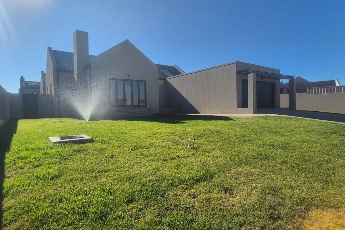 Rear view of a modern house featuring a spacious lawn, integrated sprinkler system, paved driveway, and attached garage.