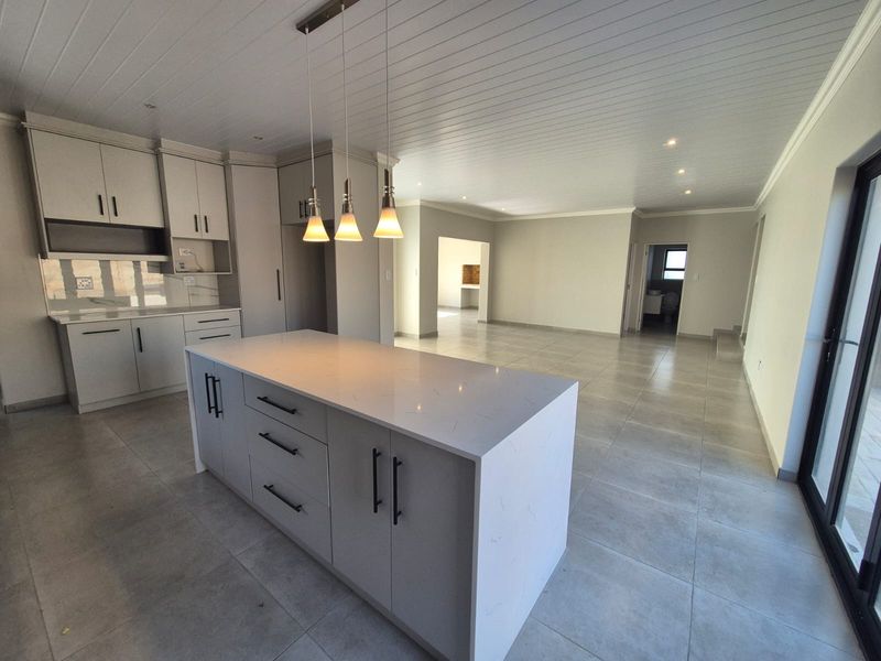 Spacious open-plan kitchen and living area featuring a central island with quartz countertops, modern cabinetry, tiled floors, and bright, neutral finishes throughout.