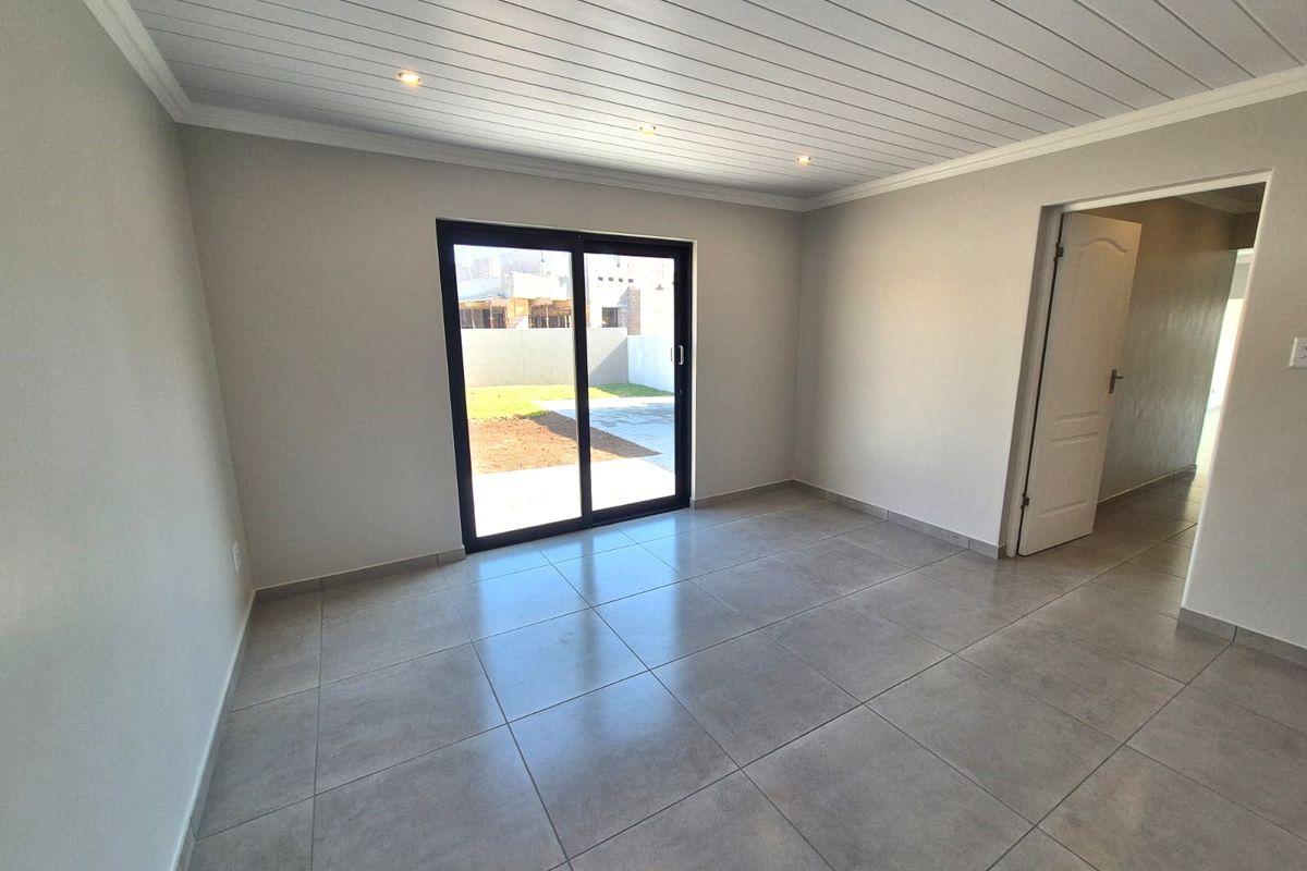 A bright, empty living room featuring large format floor tiles, a white tongue and groove ceiling with recessed lighting, and sliding doors to the garden.