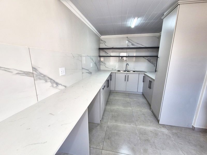 Modern, clean-lined kitchen featuring marble-look splashbacks, stone-look countertops, ample built-in cabinetry, and tiled flooring in a bright, neutral finish.