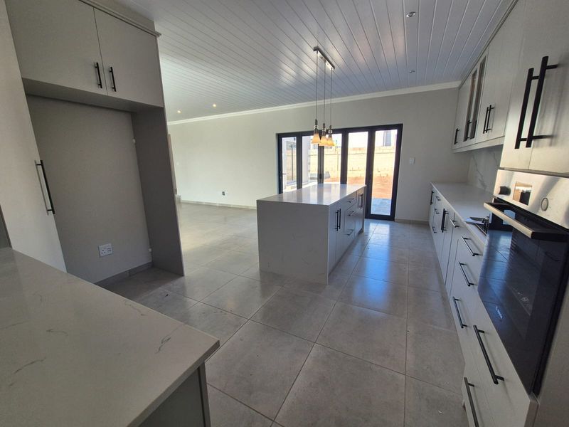Modern open-plan kitchen featuring a central island, stone countertops, built-in oven, and sleek cabinetry, flowing seamlessly into an adjacent living area with bi-fold doors.