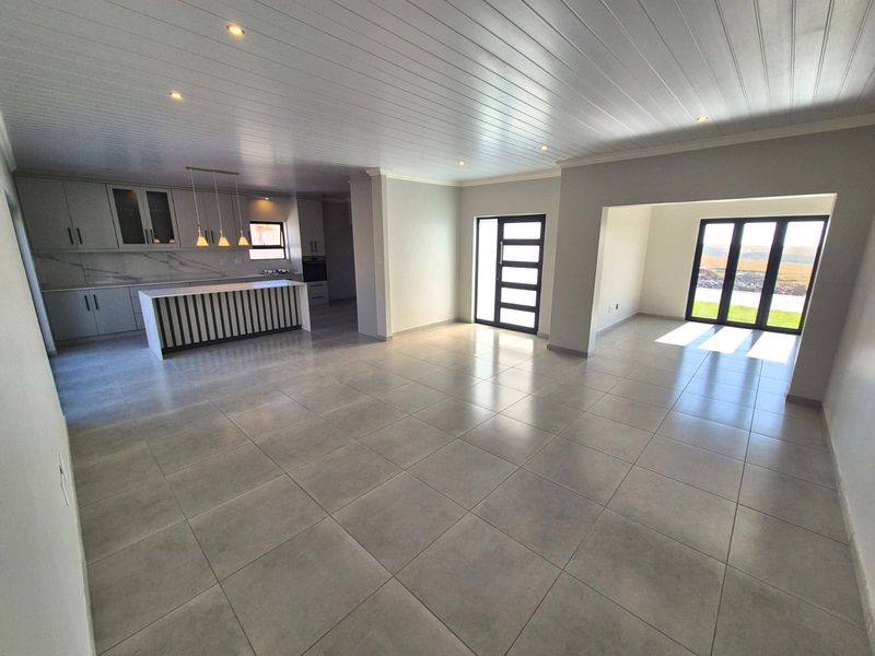 Spacious open-plan living area featuring a modern kitchen with island, tiled floors, recessed lighting, and large glass doors leading to the exterior.