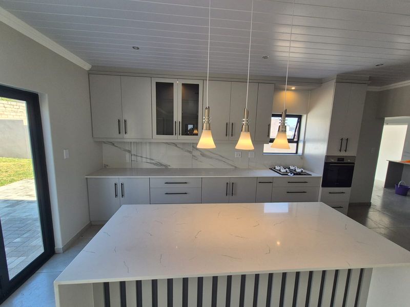 Modern kitchen featuring a large central island, quartz countertops, marble-look splashback, built-in oven, and stylish pendant lighting with a clean, contemporary finish.