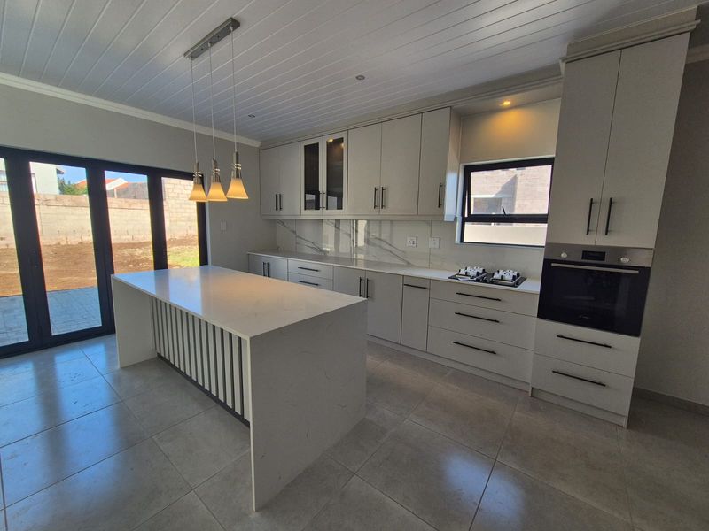 Modern kitchen featuring a central island, quartz countertops, built-in oven, gas hob, and sleek cabinetry, with direct access to the rear patio.