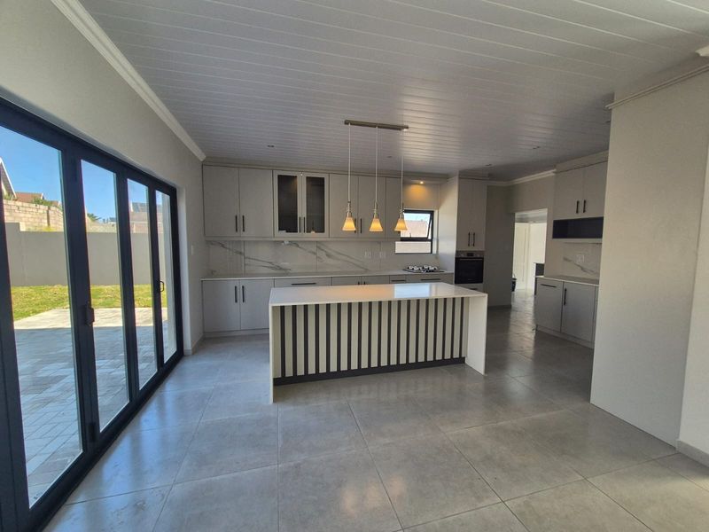 Modern open-plan kitchen featuring a central island, stone countertops, built-in cabinetry, and large sliding glass doors opening to the outdoor area.