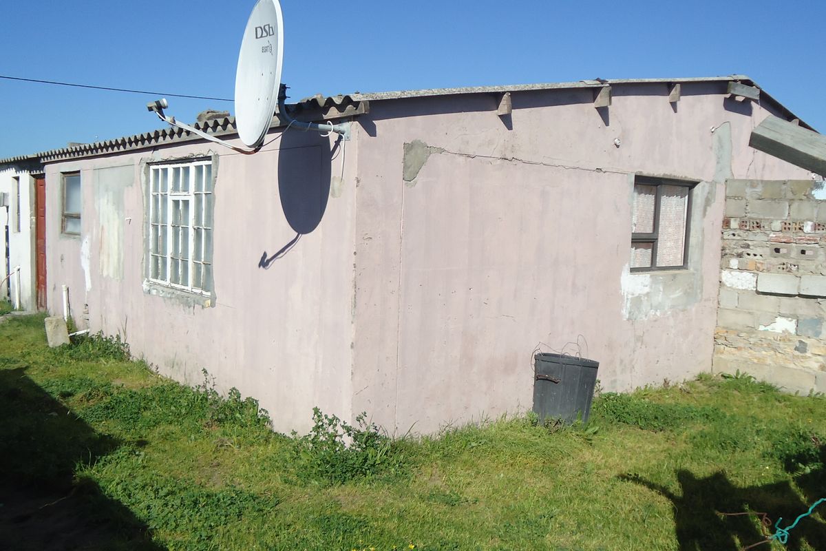 Rear exterior view of a single-story dwelling featuring a corrugated roof, satellite dishes, and visible wear to the exterior plaster and paint finishes.