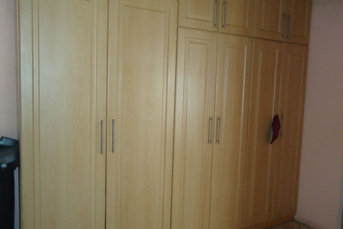 A bedroom featuring extensive light wood-finish built-in cupboards providing ample storage space.