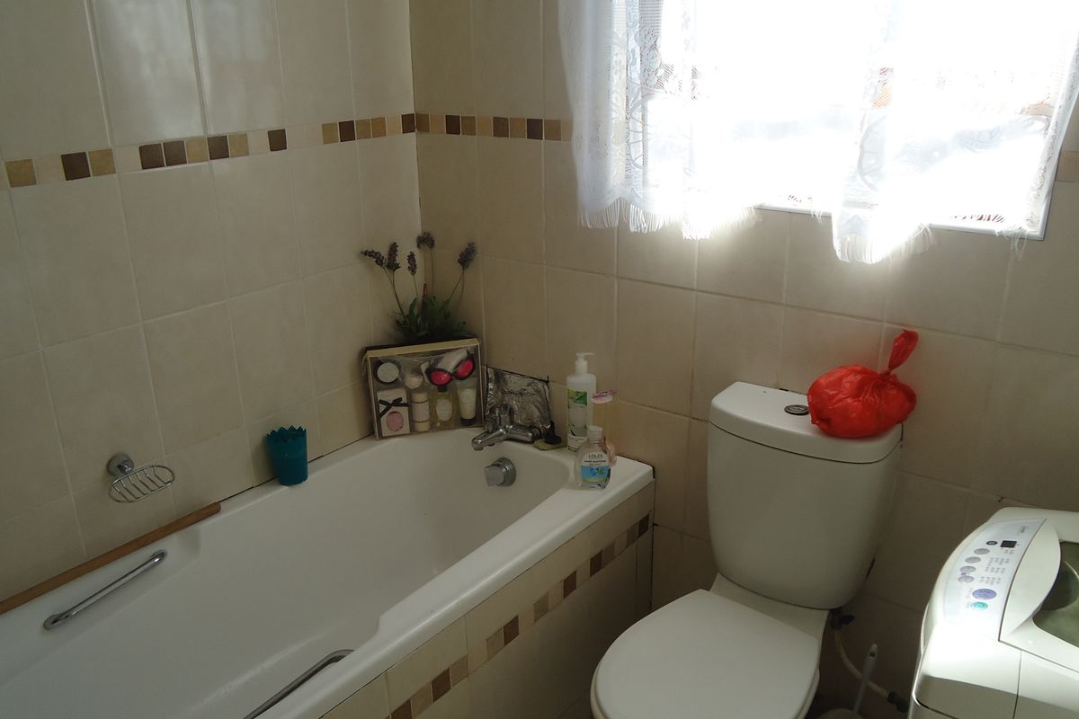 A functional bathroom featuring a built-in bathtub, toilet, and neutral ceramic wall tiling with decorative accents.