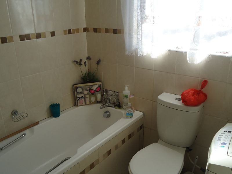 A functional bathroom featuring a built-in bathtub, toilet, and neutral ceramic wall tiling with decorative accents.