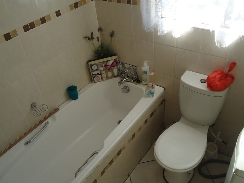 A functional bathroom featuring a bathtub with a chrome grab rail, a standard toilet, and neutral wall and floor tiling.