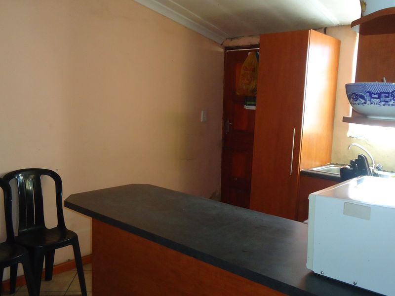 A compact kitchen area featuring built-in cabinetry, a laminate countertop, and a sink, requiring cosmetic updates to improve its overall appeal.