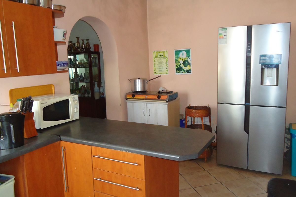 A functional kitchen featuring wood-look cabinetry, laminate countertops, and an arched doorway leading to an adjacent room, with tiled flooring throughout.