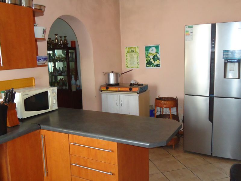 A functional kitchen featuring wood-look cabinetry, laminate countertops, and an arched doorway leading to an adjacent room, with tiled flooring throughout.