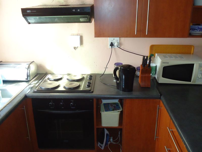 A compact kitchen featuring wooden cabinetry, laminate countertops, a built-in oven, electric hob, and an extractor fan.