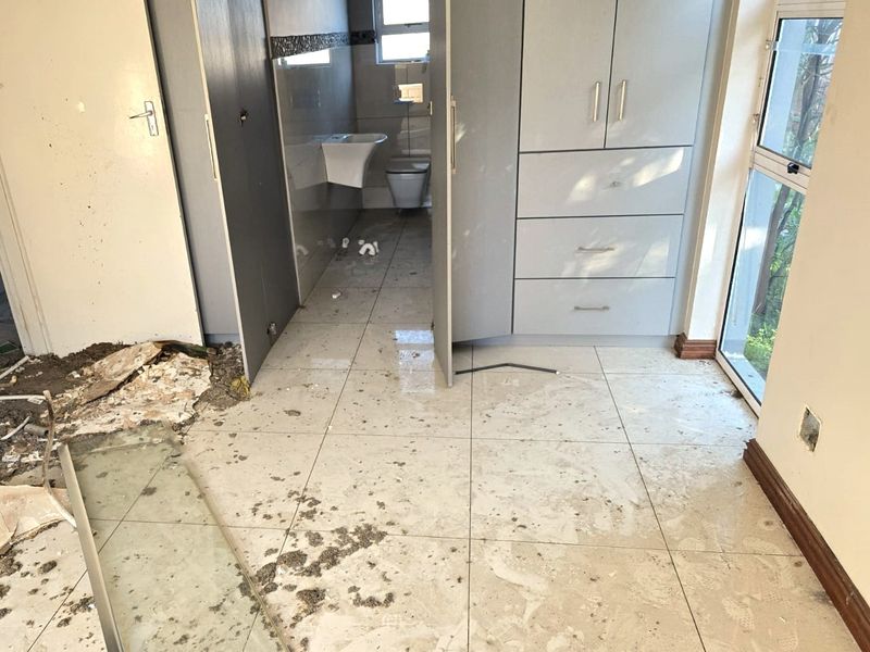 A bathroom space currently undergoing renovation, featuring built-in cabinetry, tiled flooring, and basic sanitary fixtures, requiring significant cleaning and finishing work.