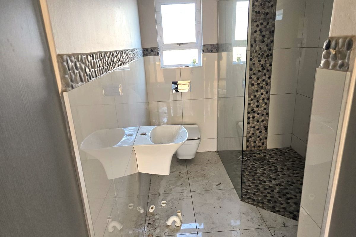 A bathroom in need of completion, featuring a glass shower enclosure, wall-mounted toilet, and pebble tile accents, currently missing a vanity basin.