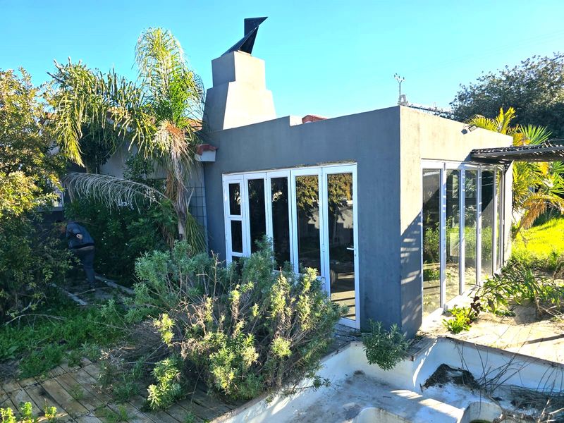 Rear exterior view featuring a modern structure with bi-fold doors, an external fireplace, and an adjacent swimming pool area requiring maintenance.