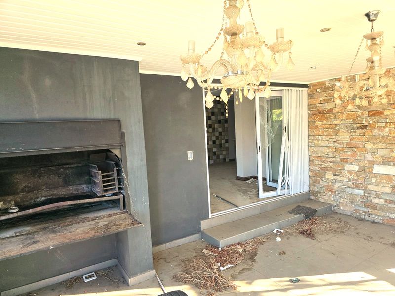 Covered patio area featuring a built-in braai, stone feature wall, and sliding door access to the interior. Requires maintenance and repair.