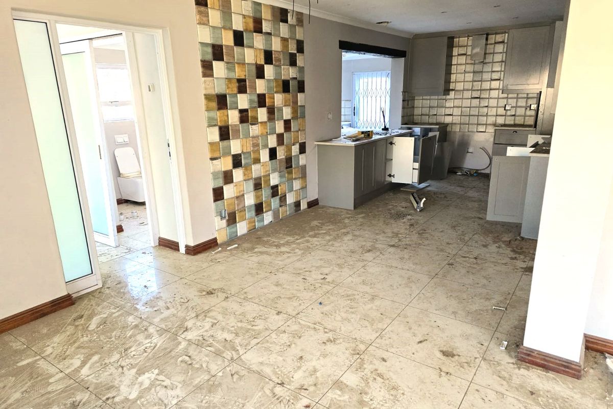 An unfinished kitchen area featuring tiled floors, a mosaic feature wall, and cabinetry in the process of installation or renovation.