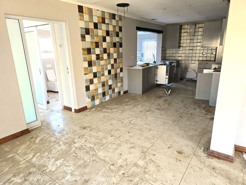 An unfinished kitchen area featuring tiled floors, a mosaic feature wall, and cabinetry in the process of installation or renovation.