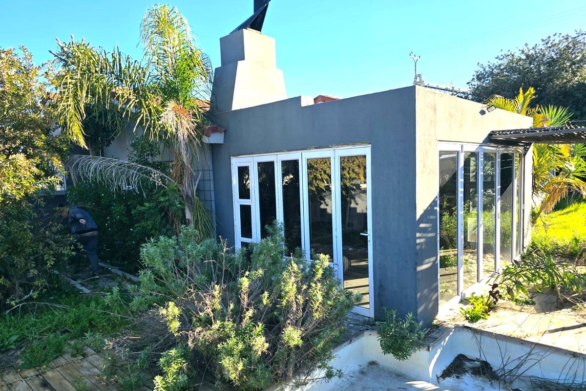 Rear exterior view featuring a modern structure with bi-fold doors, an external fireplace, and an adjacent swimming pool area requiring maintenance.