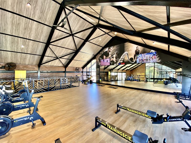 A modern, well-maintained gym featuring high vaulted ceilings with exposed steel trusses, brick feature walls, and expansive wall mirrors.
