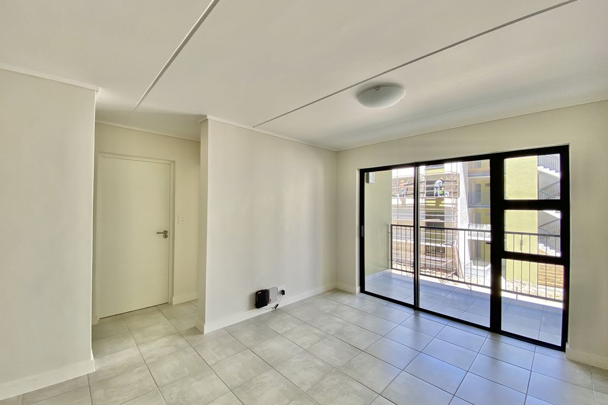 A bright, empty living area featuring neutral tiled flooring and a large sliding glass door providing access to an outdoor balcony.