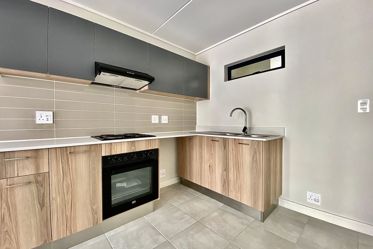 Modern kitchen featuring wood-grain lower cabinets, dark grey upper cabinetry, built-in oven, hob, extractor fan, and neutral tiled finishes.