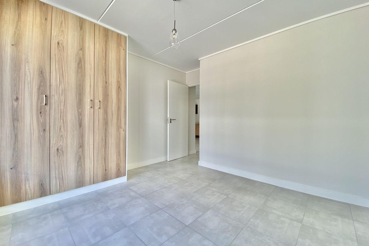 A bright, empty bedroom featuring modern wood-finish built-in wardrobes and neutral tiled flooring, offering a clean and versatile space.
