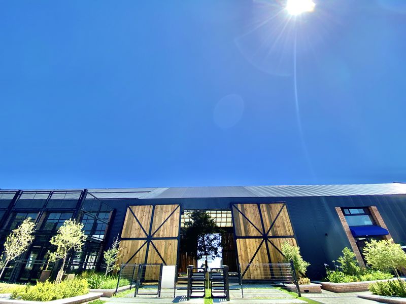 Modern industrial-style apartment building facade featuring corrugated metal cladding, large timber barn-style entrance doors, and manicured garden landscaping.