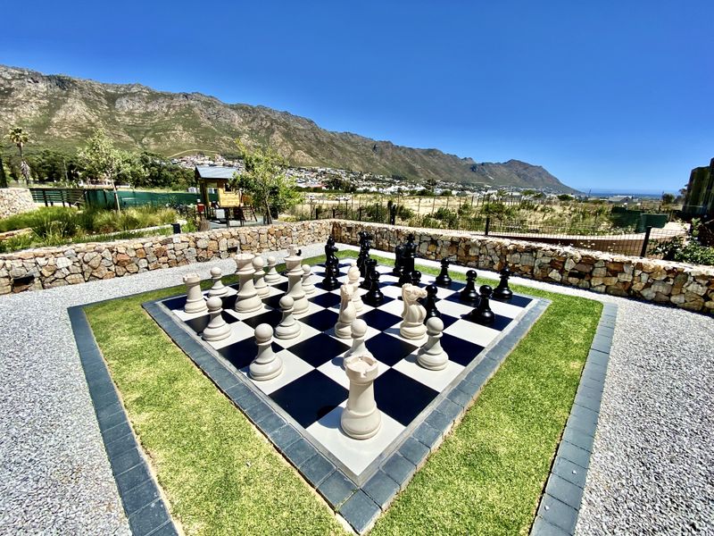 A well-maintained outdoor garden area featuring a large permanent chess board set within a landscaped lawn and stone retaining walls.