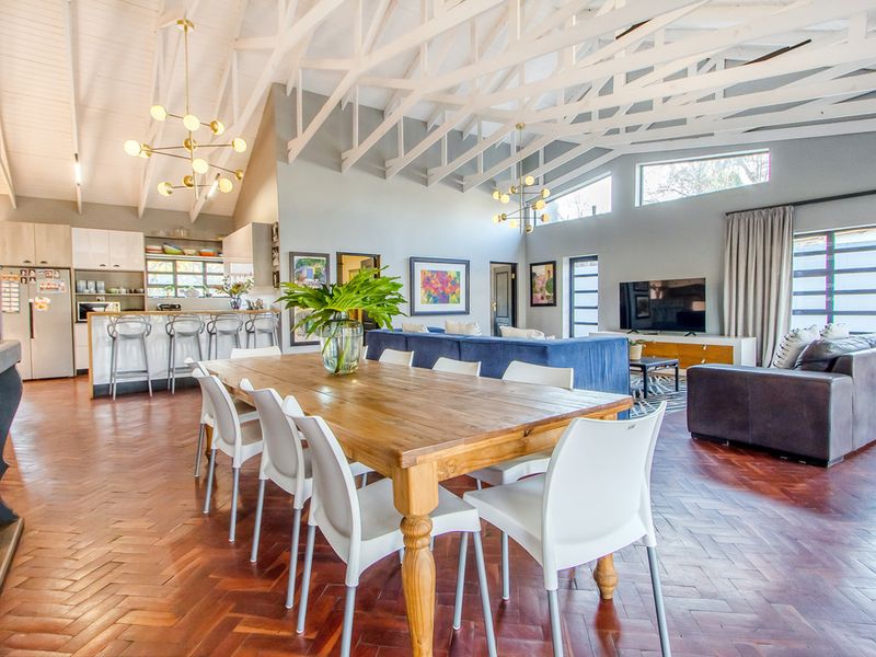 Spacious open-plan living, dining, and kitchen area featuring high vaulted ceilings with exposed white trusses and classic herringbone parquet flooring.