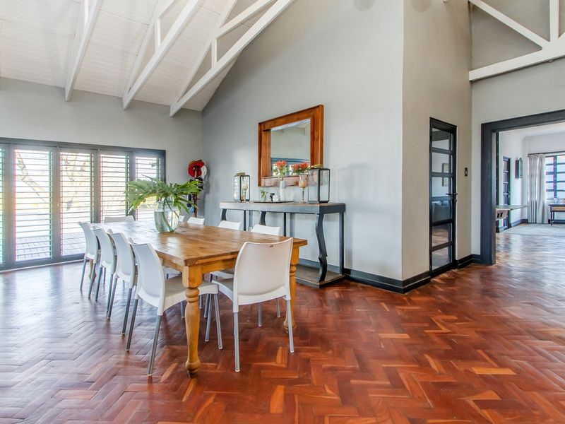 Spacious dining room featuring elegant herringbone parquet flooring, a high vaulted ceiling with exposed timber trusses, and large sliding doors opening to the exterior.