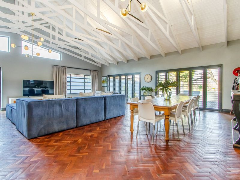 Spacious open-plan living and dining area featuring high vaulted ceilings with exposed white trusses, elegant herringbone parquet flooring, and large aluminium stacker doors.