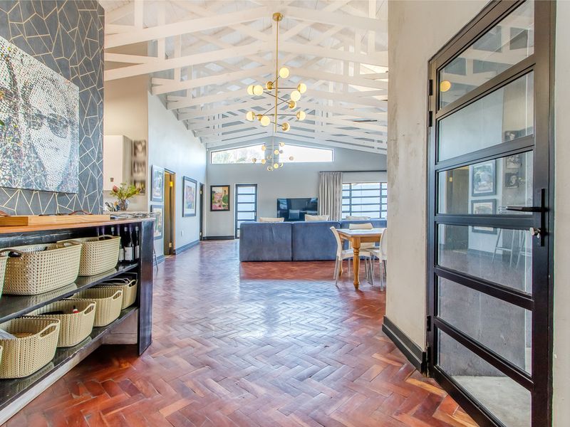 Spacious open-plan living area featuring striking herringbone parquet flooring, exposed white timber trusses, and a modern industrial-style glass door.