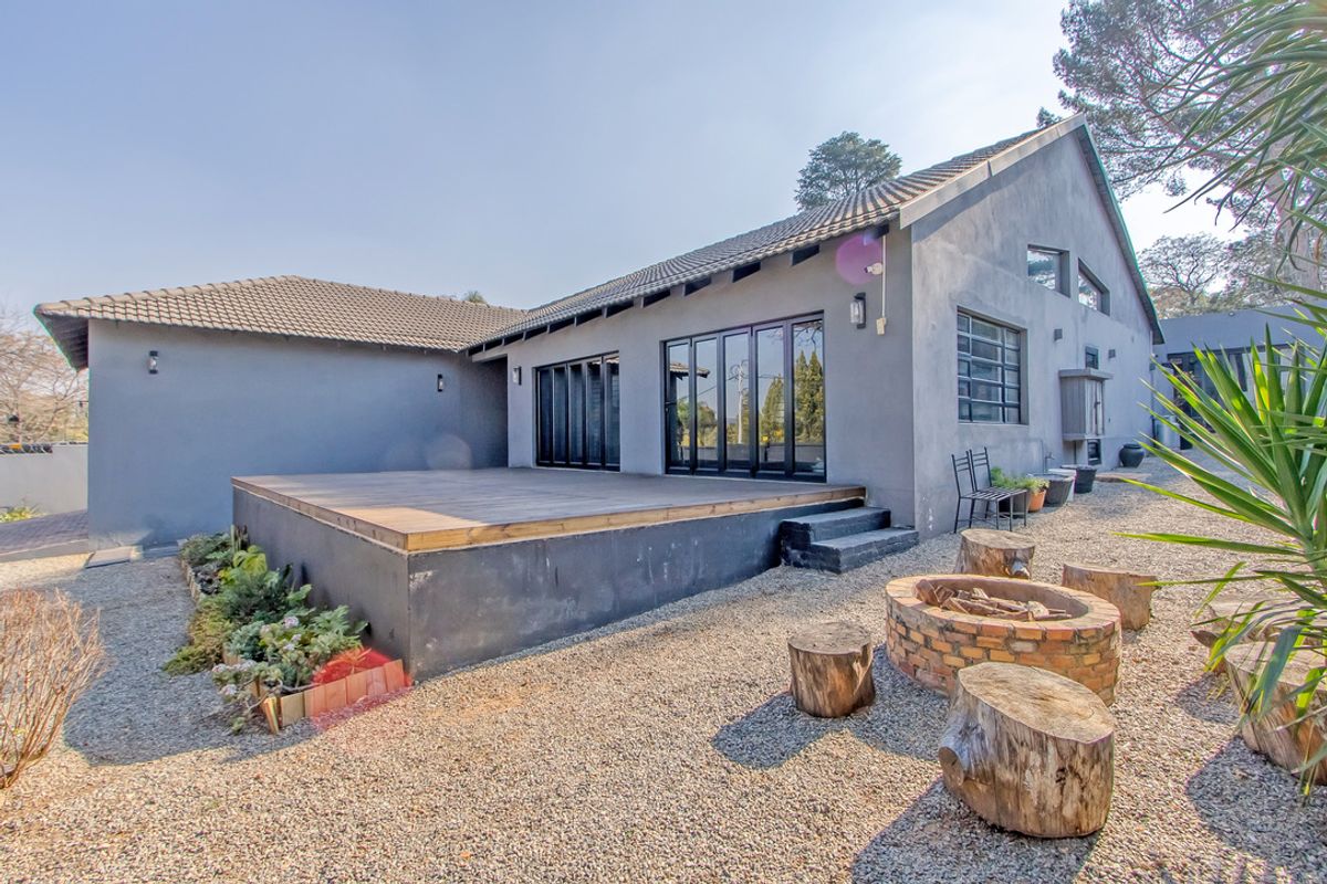 Rear view of the property featuring a raised timber deck, black aluminium folding doors, and a brick fire pit in a gravel garden setting.