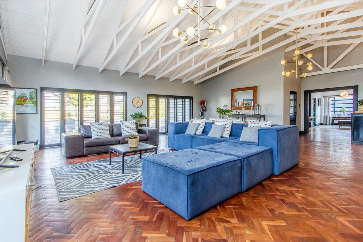 Spacious living area featuring high vaulted ceilings with exposed white timber trusses, elegant herringbone parquet flooring, and large aluminium stacker doors leading outdoors.