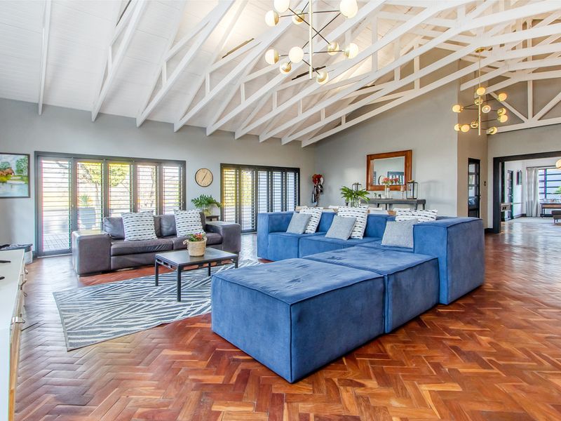 Spacious living area featuring high vaulted ceilings with exposed white timber trusses, elegant herringbone parquet flooring, and large aluminium stacker doors leading outdoors.