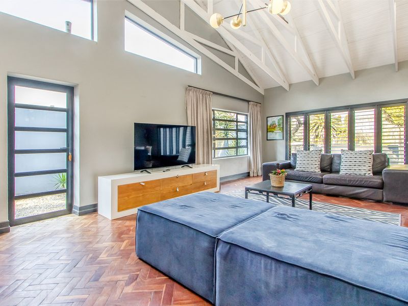 Spacious living room featuring high vaulted ceilings with exposed white trusses, herringbone parquet flooring, and large windows providing ample natural light.