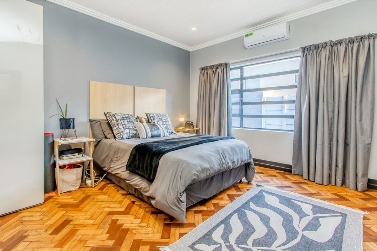 A well-maintained bedroom featuring classic herringbone parquet flooring, a split-system air conditioner, and built-in wardrobe storage.