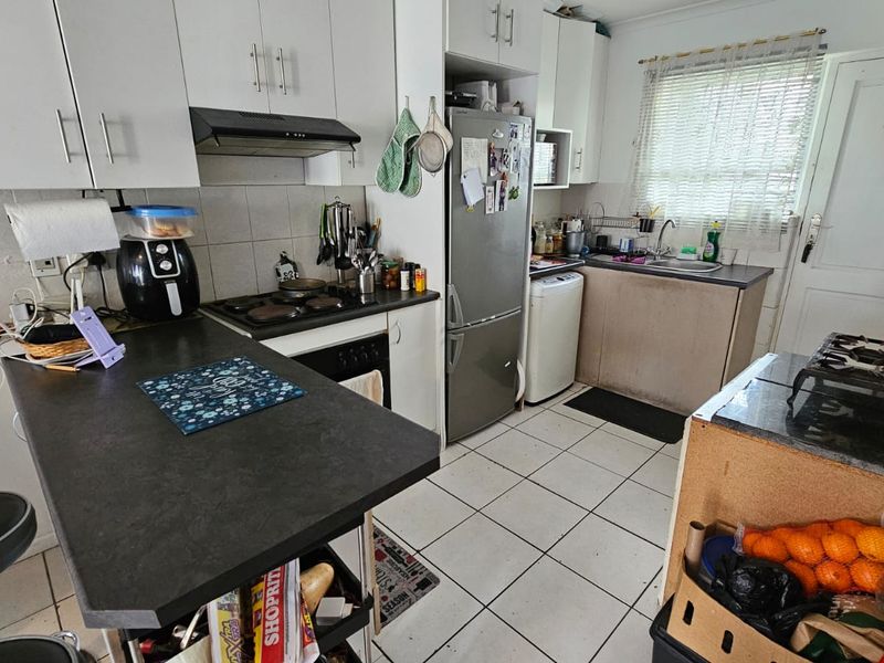 Functional kitchen featuring white cabinetry, dark laminate countertops, integrated hob and oven, and tiled flooring, offering a practical layout for daily meal preparation.